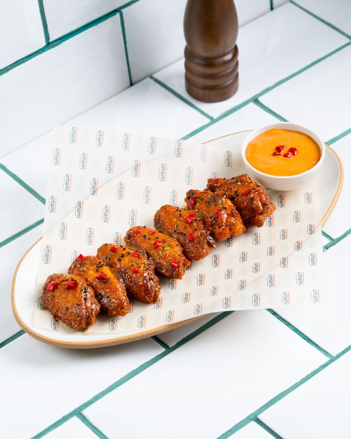 A row of chicken wings in a glossy mango habanero glaze flecked with red chilli, served with a pot of orange dipping sauce.