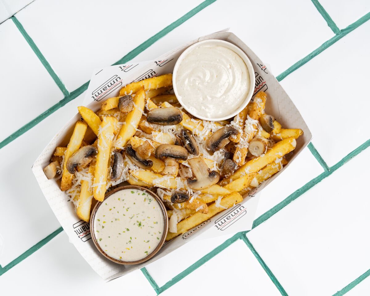 Fries tossed with sauteed mushrooms in a creamy truffle sauce, served with a pot of white dip, shot from directly overhead.