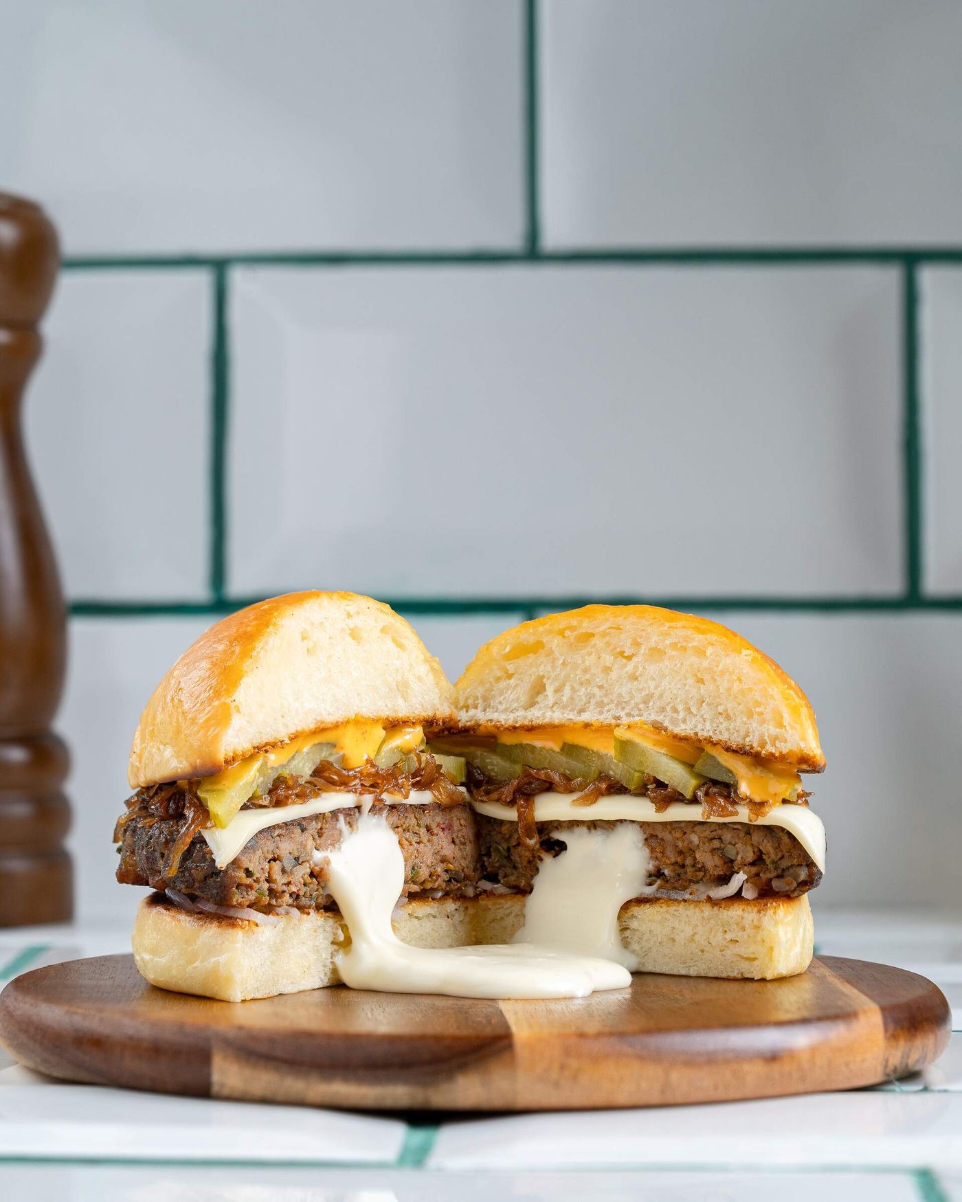A thick fire-grilled patty filled with molten white cheese, cut in half so the cheese pours out onto the board, layered with caramelised onion, pickles and melted cheese in a soft milk bun.